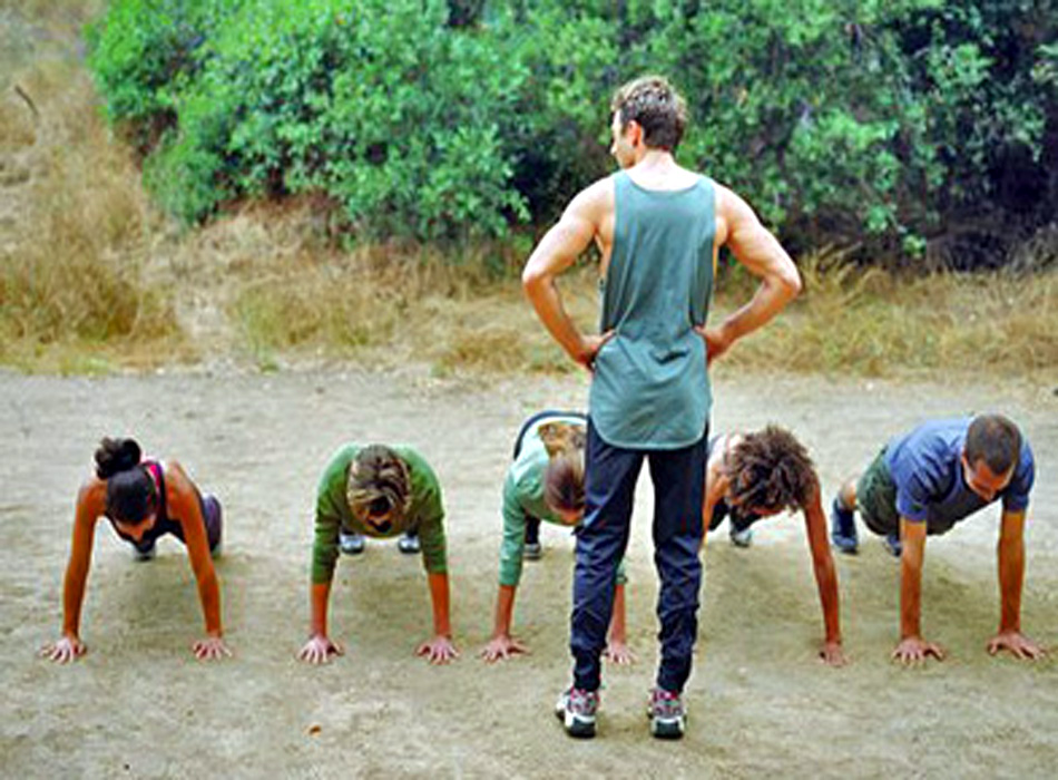 Man standing over group of people doing pushups, rear view